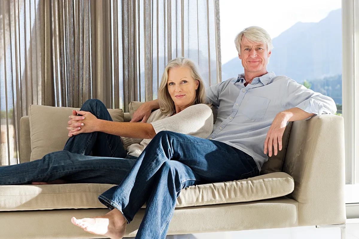 Pareja adulta en el sofá de su nueva casa con un gran ventanal con vistas a la naturaleza